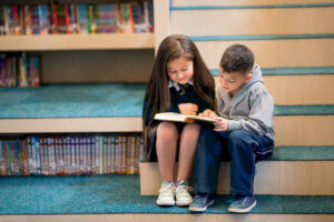 2 young students reading together on the library stairs