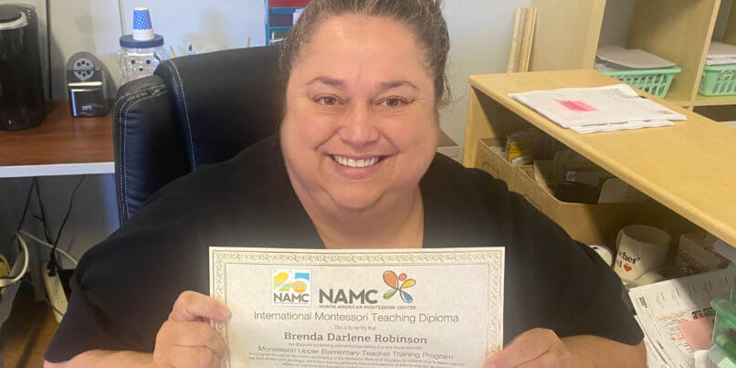 Ms. Brenda completed her official NAMC training. Picture of her holding her certification in her classroom.