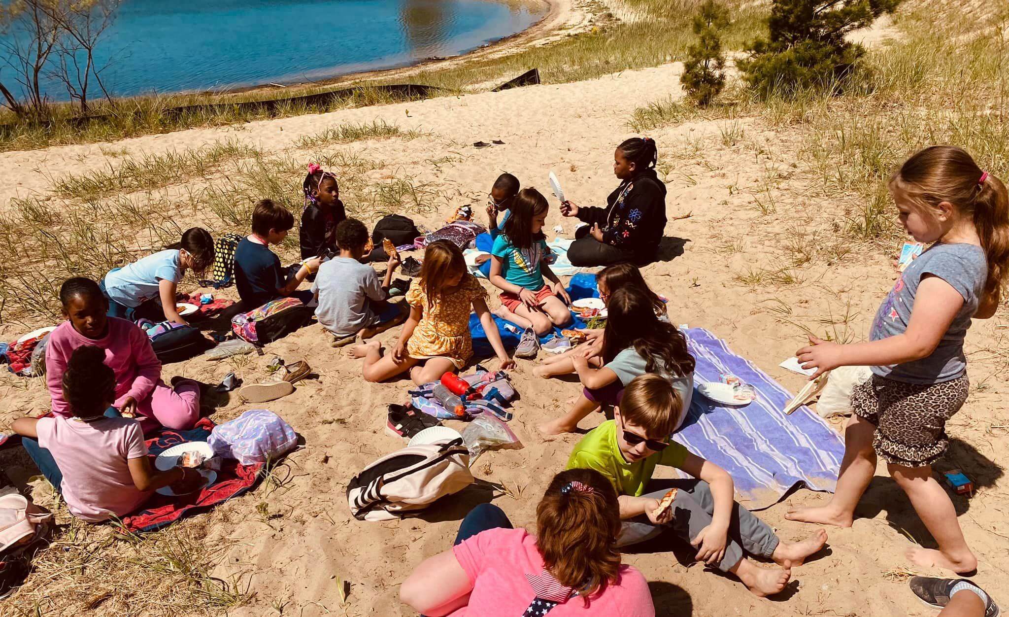 MMAEC students lay in the sand working with families on a field trip to the beach